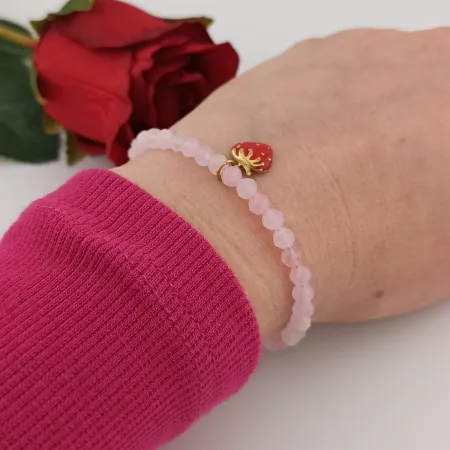 Romantyczna bransoletka z różowymi koralikami i zawieszką truskawką elegancko prezentująca się na ręku modelki