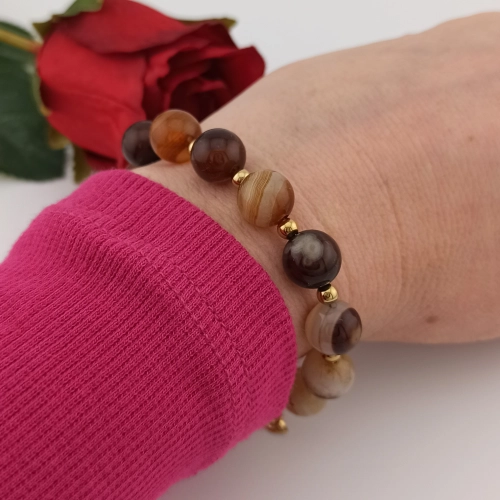Wyrazista bransoletka z dużym brązowym agatem w złotej oprawie elegancko zaprezentowana na ręku kobiety. Wyrazista bransoletka z dużym brązowym agatem w złotej oprawie elegancko zaprezentowana na ręku kobiety.
