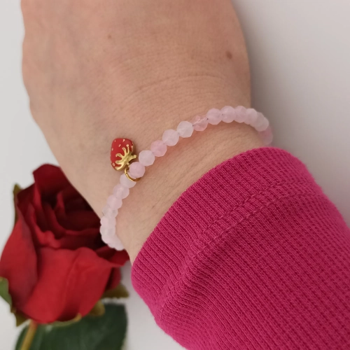 Romantyczna bransoletka z różowymi koralikami i zawieszką truskawką elegancko prezentująca się na ręku modelki